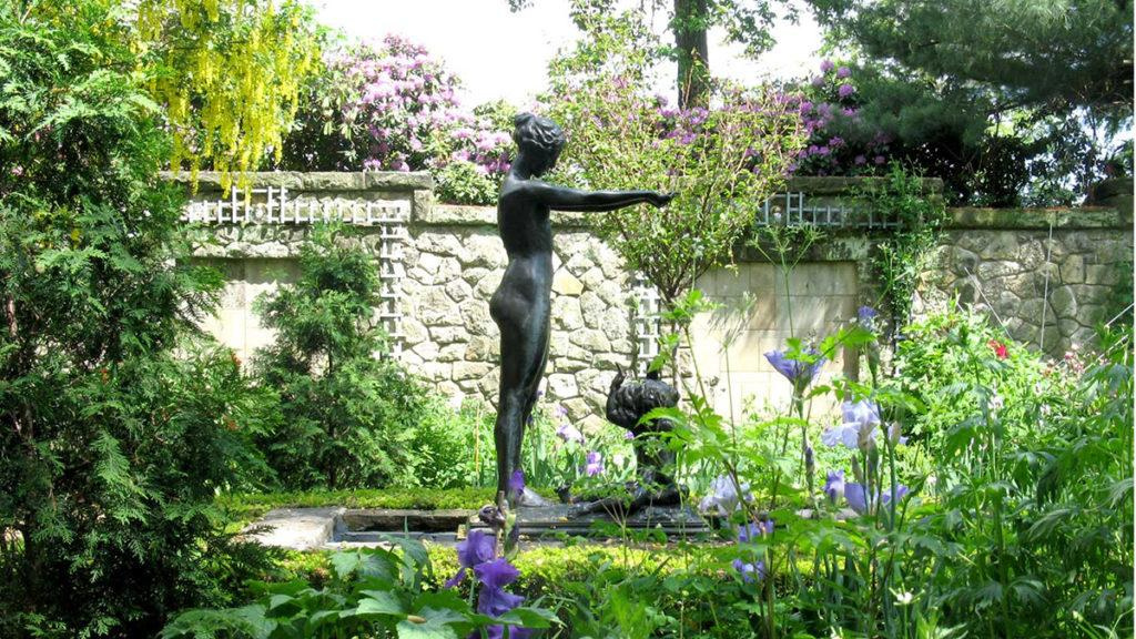 Green Outdoor landscape garden featuring different plants and a black stone sculpture of a female in the center.