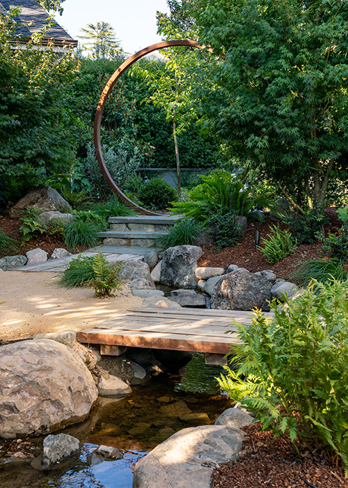 stream with bridge and pathway with moon gate in background